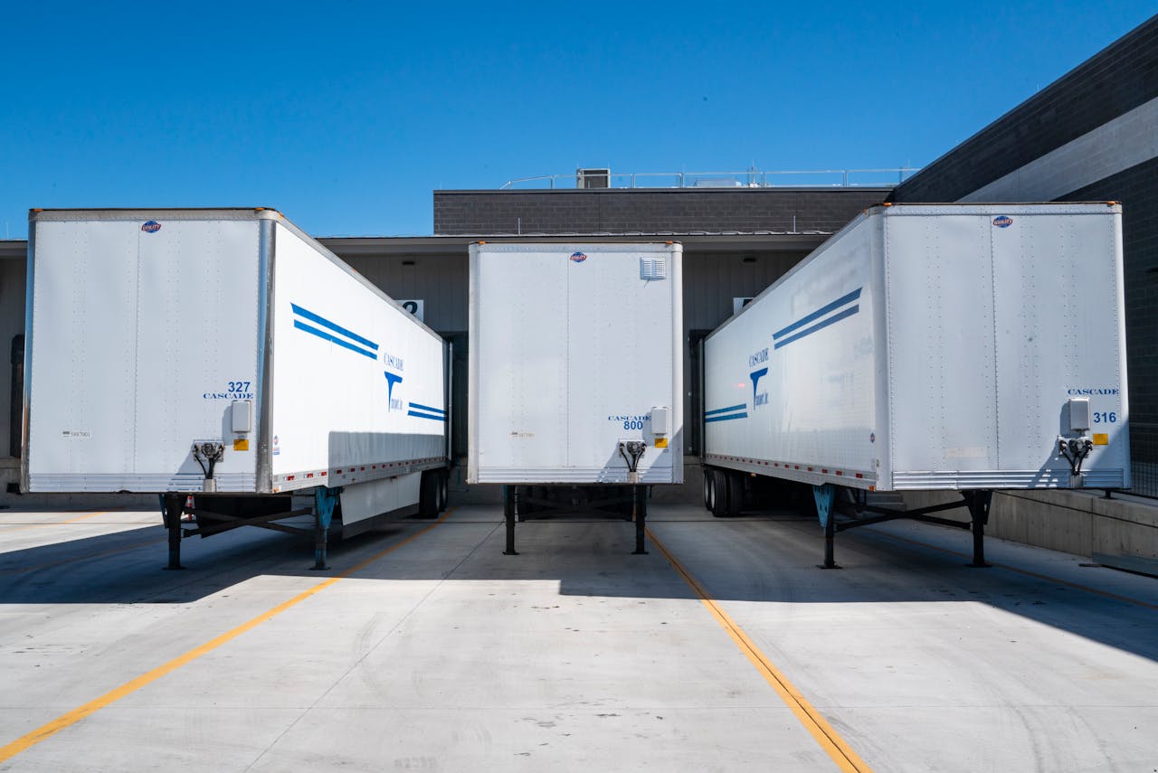 services-03 Three white cargo trailers parked at an industrial shipping dock under clear blue skies.